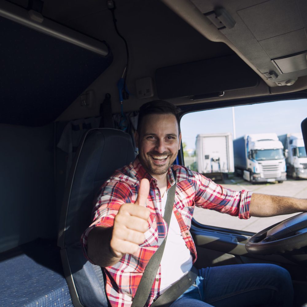 Portrait of professional motivated truck driver holding thumbs up in truck cabin. Portrait of professional motivated truck driver holding thumbs up in truck cabin.